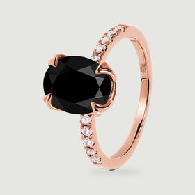 The rose gold ring stands at an angle with the black stone, curved prongs and open inner band visible.