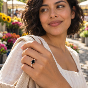 A woman wears the rose gold black stone ring while holding a woven bag strap at a sunlit flower market.