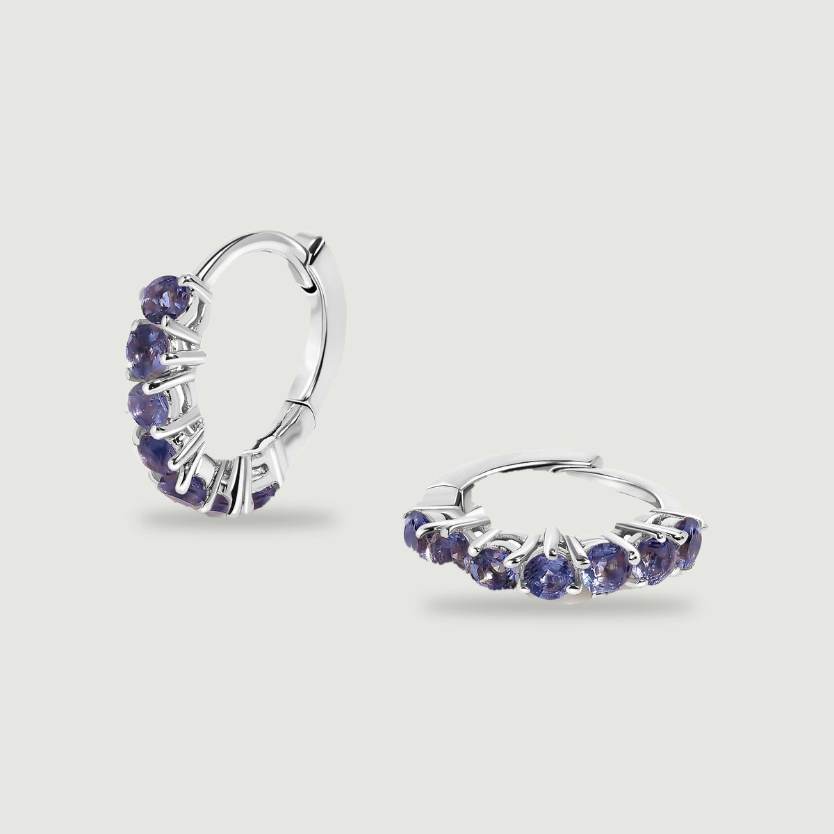 Two silver-tone hoops with round violet stones are arranged upright and flat on a light gray surface.