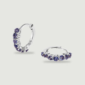 Two silver-tone hoops with round violet stones are arranged upright and flat on a light gray surface.