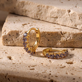 One yellow gold-tone hoop stands beside a second hoop lying on a beige stone tabletop.