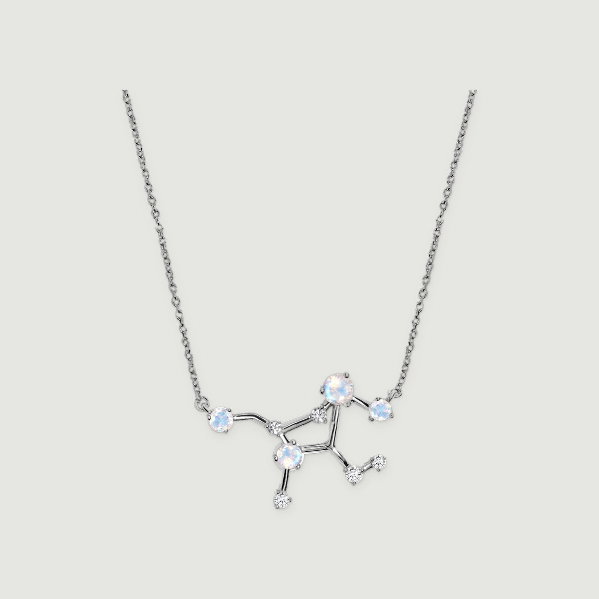 A silver necklace with an open constellation centre, round pale stones and small clear stones rests on a light grey background.