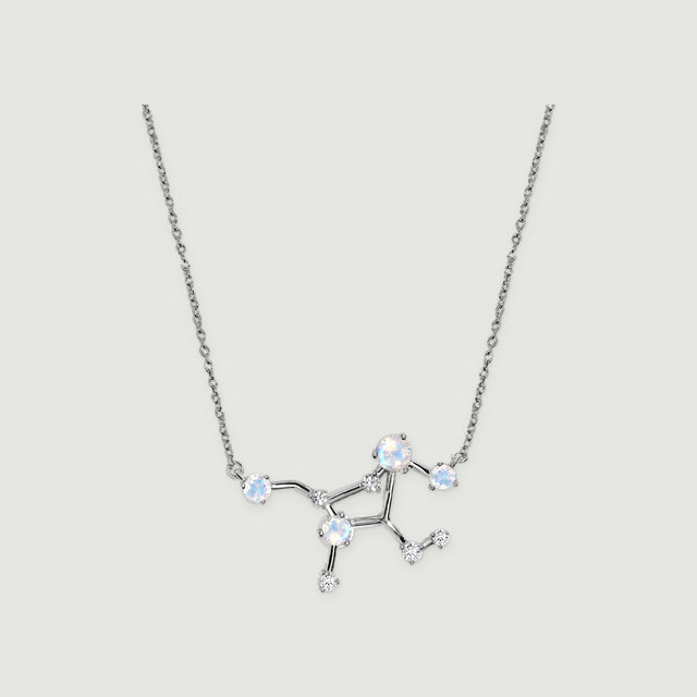 A silver necklace with an open constellation centre, round pale stones and small clear stones rests on a light grey background.