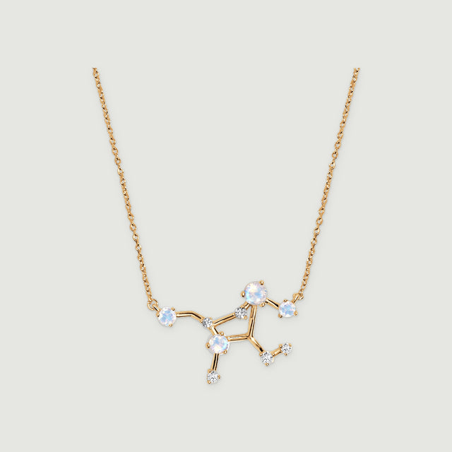 A yellow gold necklace displays a branching constellation centre with pale round stones against a light grey surface.