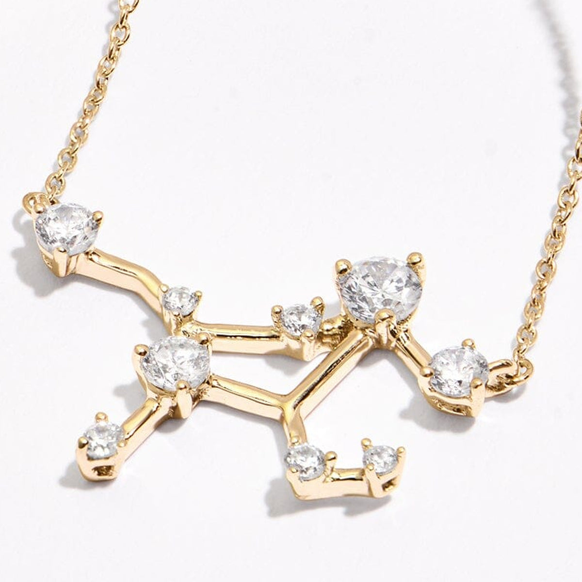 An angled view of a yellow gold constellation necklace shows raised round stone settings and fine chain links on a clean pale tabletop.