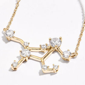 An angled view of a yellow gold constellation necklace shows raised round stone settings and fine chain links on a clean pale tabletop.
