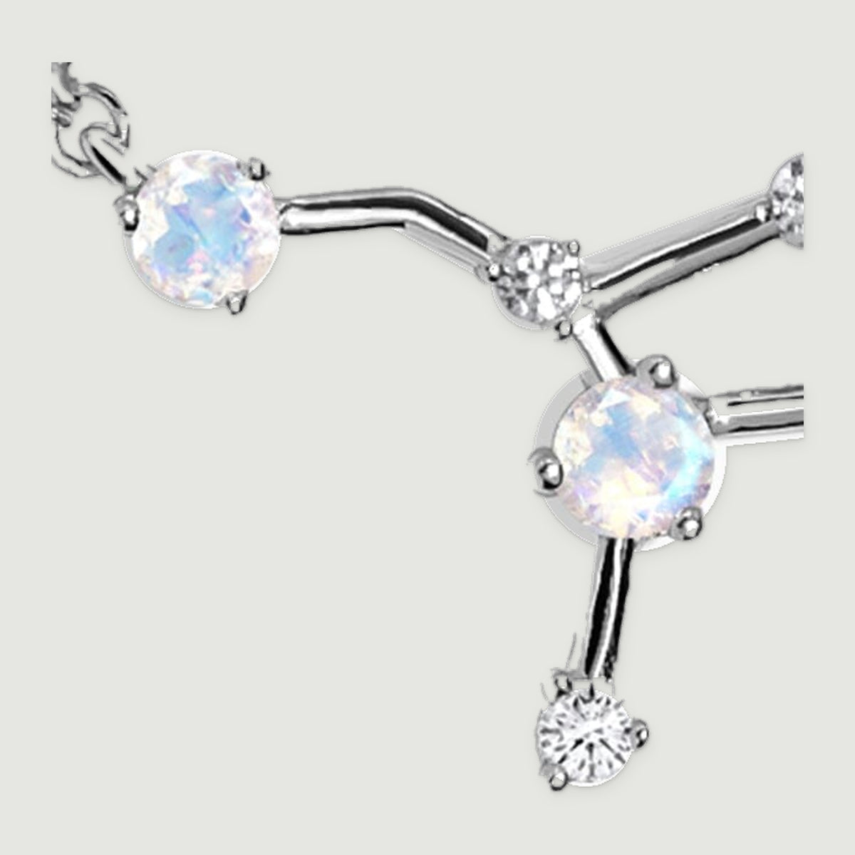 A magnified silver necklace detail shows two pale round stones, small clear stones and the lower polished branching arm.
