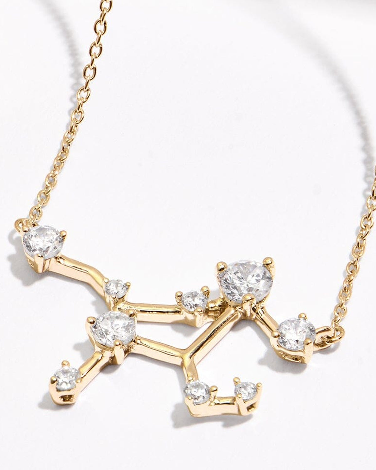 A yellow gold constellation necklace lies on a pale tabletop with two fine chain sections extending above its open stone-set centre.