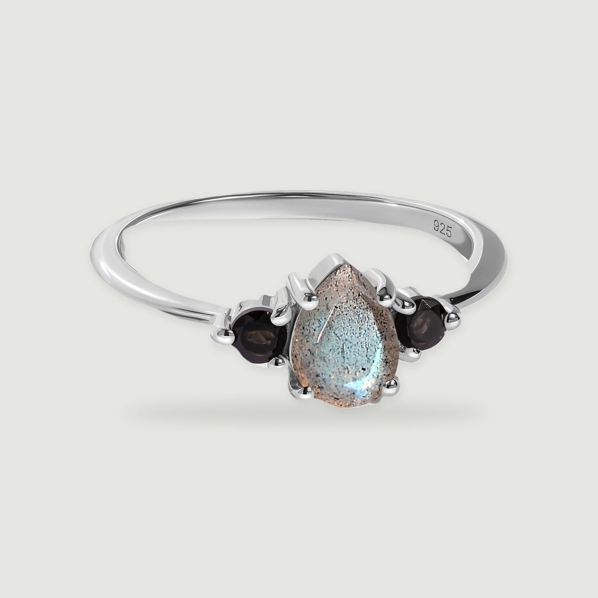 A sterling silver ring with a pear-shaped labradorite and two round black obsidian stones rests on a light gray surface.