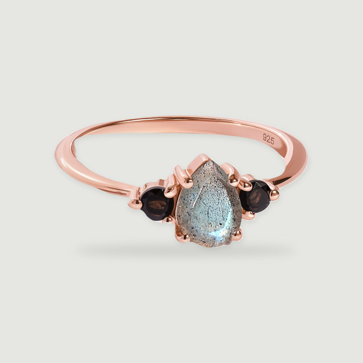 A rose gold vermeil ring shows a blue-gray pear-shaped stone between two dark round stones on a light gray background.