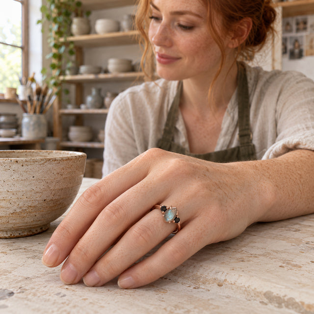 The rose gold vermeil ring is shown on a freckled hand beside a ceramic bowl on a pottery studio workbench.