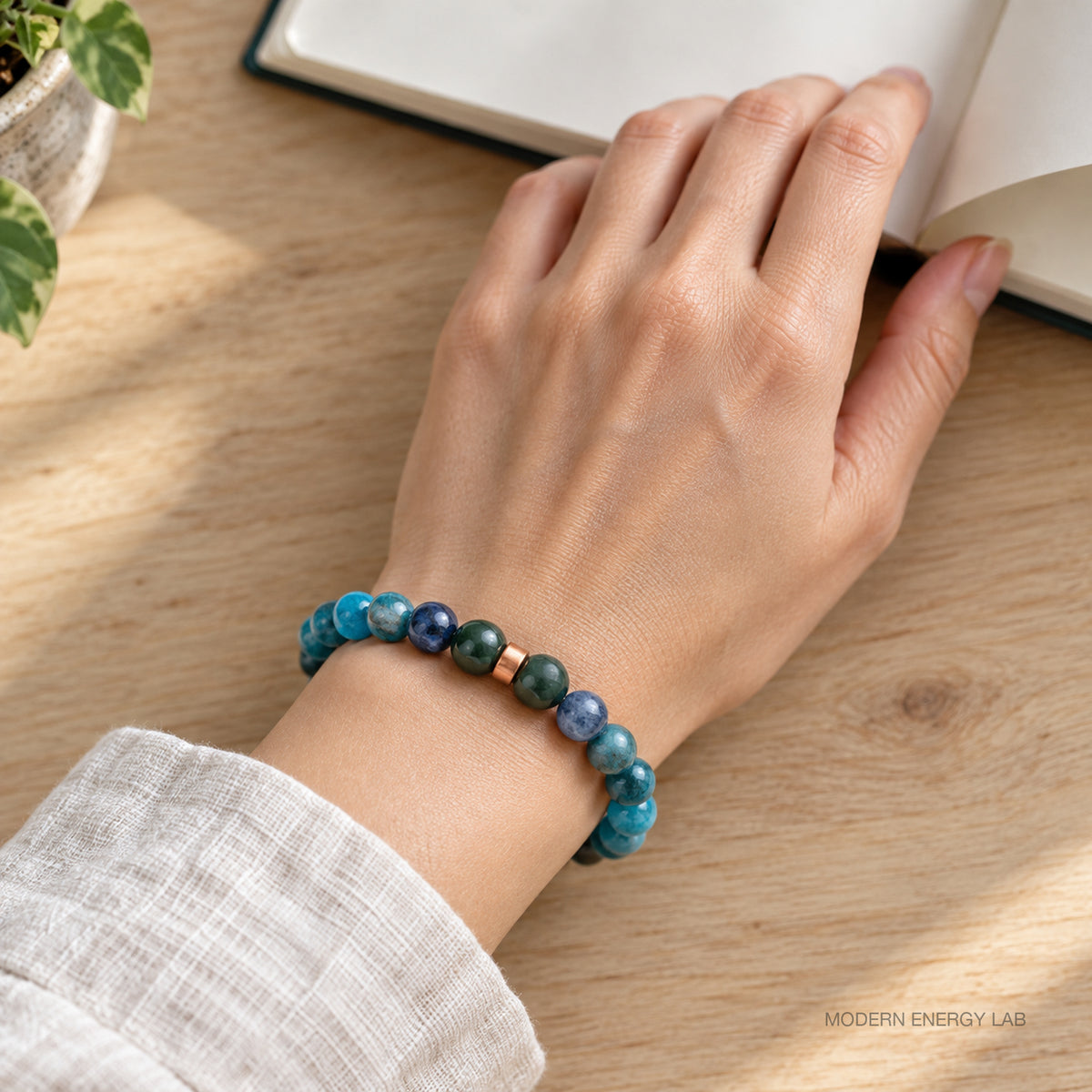 Blue-green bracelet on a wrist beside an open notebook on an oak table