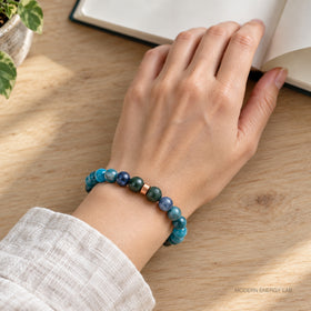 Blue-green bracelet on a wrist beside an open notebook on an oak table