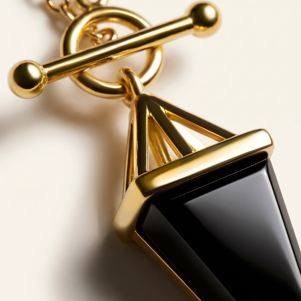 An angled close-up shows the polished gold setting, circular clasp, and glossy black stone on a pale surface.