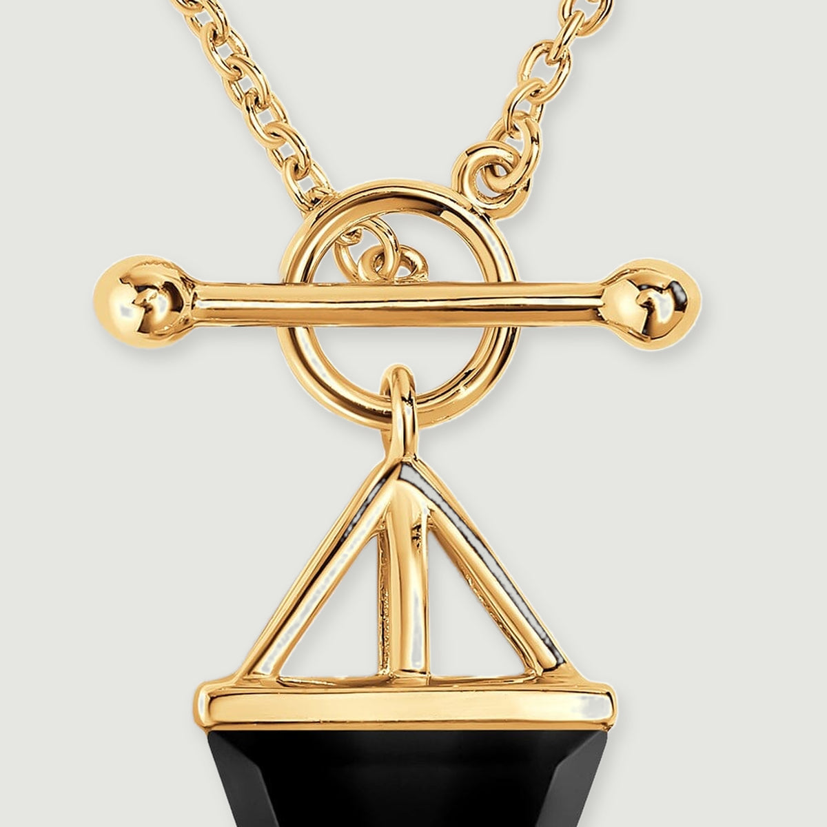 A circular gold clasp and a horizontal bar sit above the open triangular pendant setting.