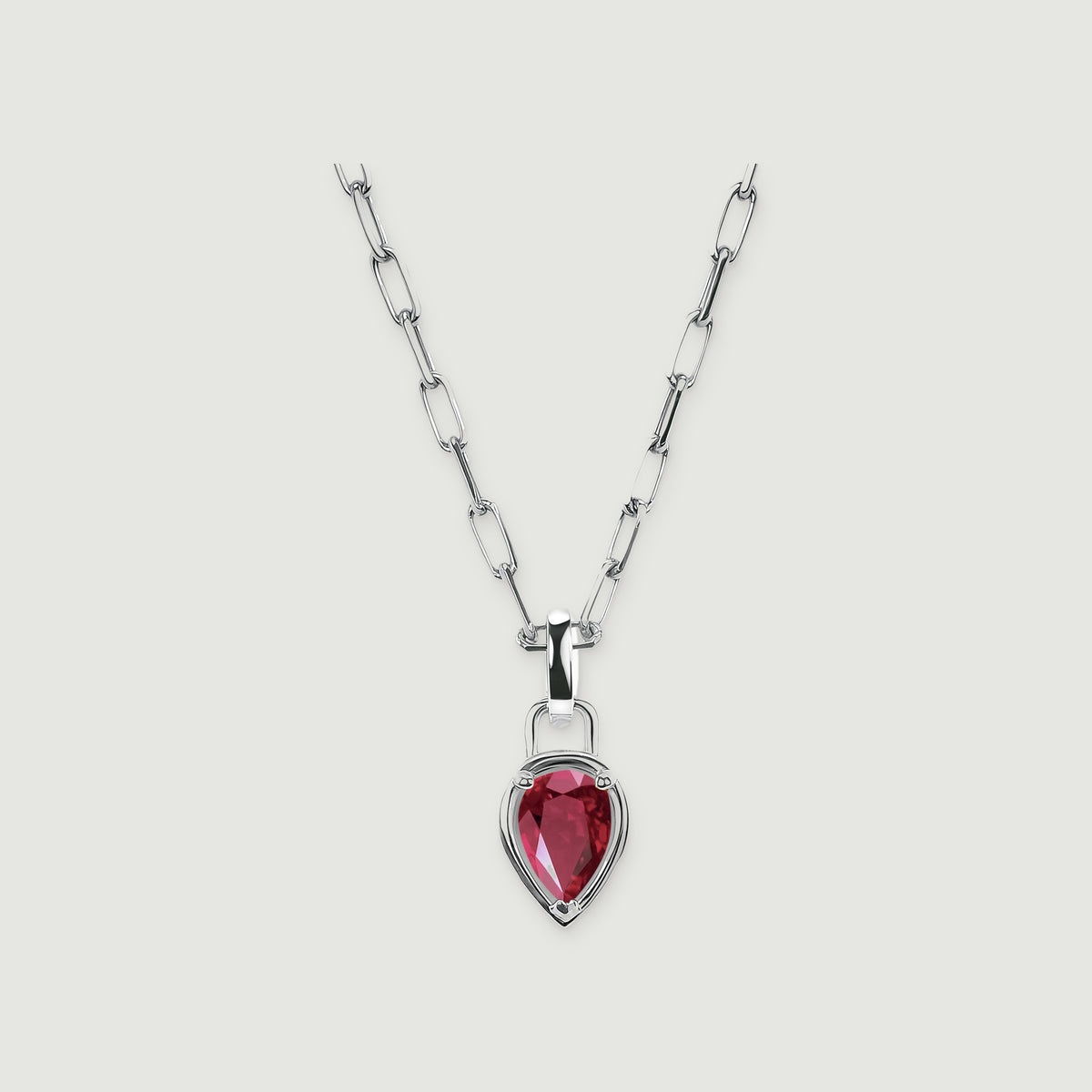 A red pear-shaped ruby sits in a polished silver-colored setting below an open-link chain on a light gray surface.