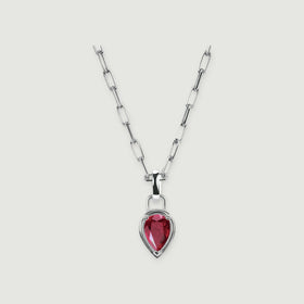 A red pear-shaped ruby sits in a polished silver-colored setting below an open-link chain on a light gray surface.