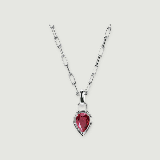 A red pear-shaped ruby sits in a polished silver-colored setting below an open-link chain on a light gray surface.