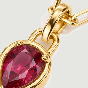 A close view shows red gemstone facets, rounded gold prongs, and a broad polished pendant bail.