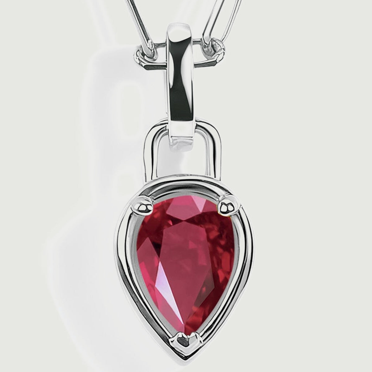 The pointed red ruby pendant is shown close up with silver-colored prongs and a smooth reflective bail.
