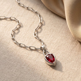 A silver-colored link chain curves across cream fabric toward a red pear-shaped pendant.