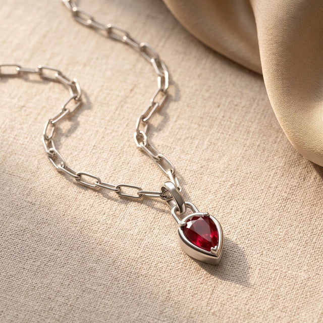 A silver-colored link chain curves across cream fabric toward a red pear-shaped pendant.