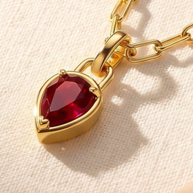An angled close view reveals the gold side wall around the red stone and the connecting pendant loop on cream fabric.