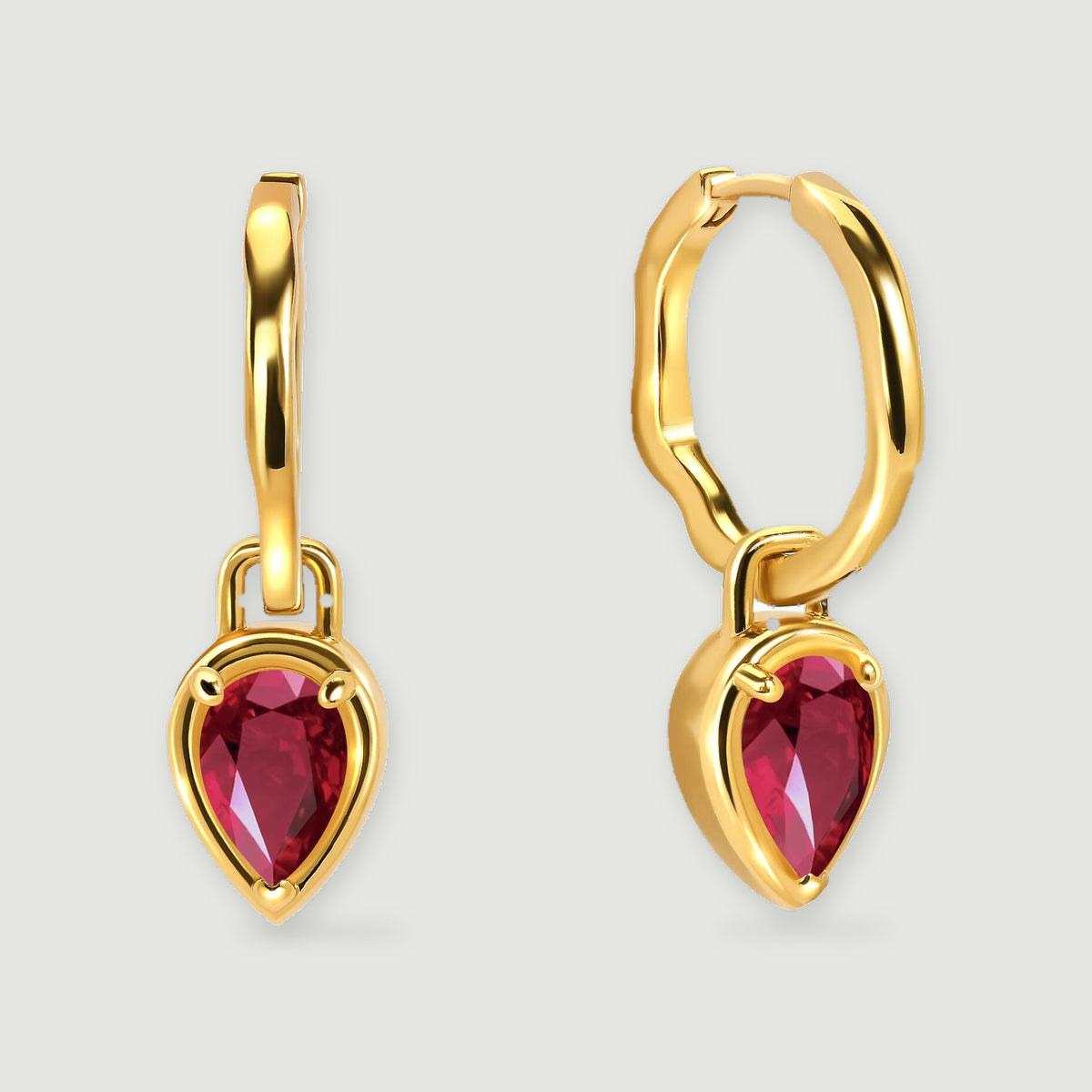 A pair of yellow gold plated hoops with red pear-shaped drops is centered on a light gray background.