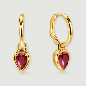 A pair of yellow gold plated hoops with red pear-shaped drops is centered on a light gray background.