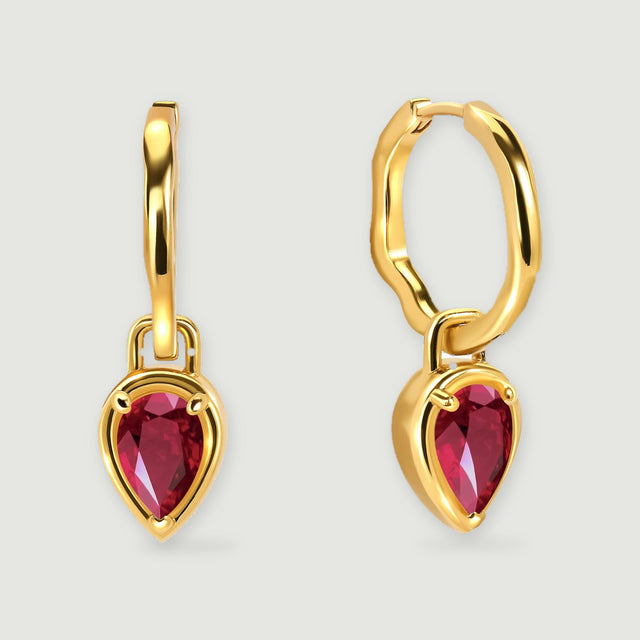 A pair of yellow gold plated hoops with red pear-shaped drops is centered on a light gray background.