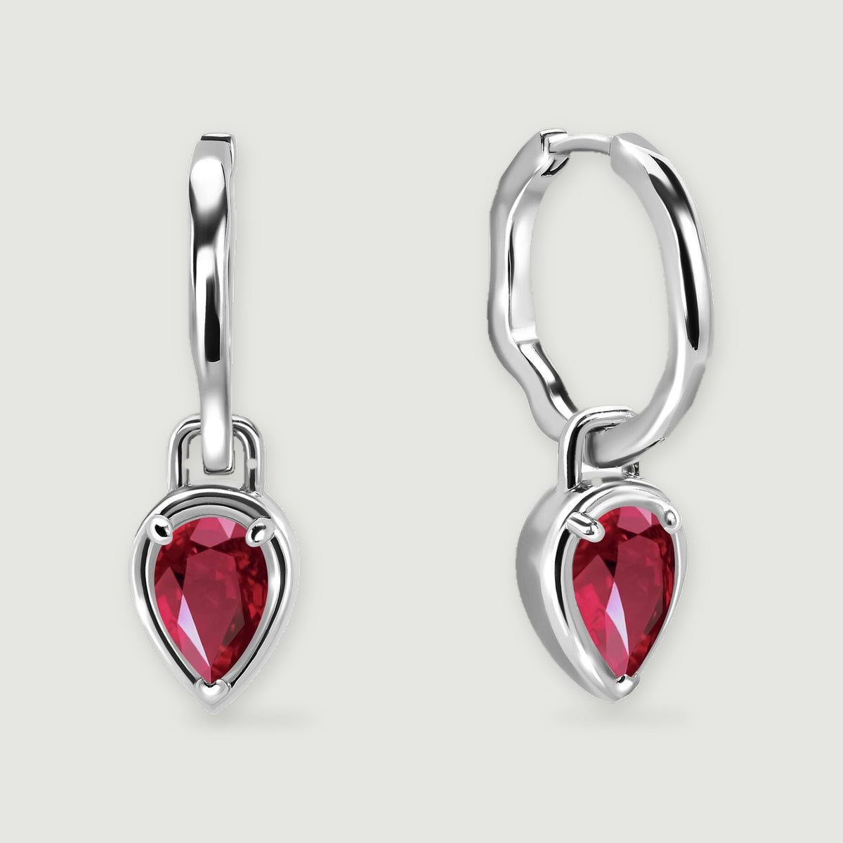 Two white rhodium plated hoop earrings display red pear-shaped stones above soft shadows.