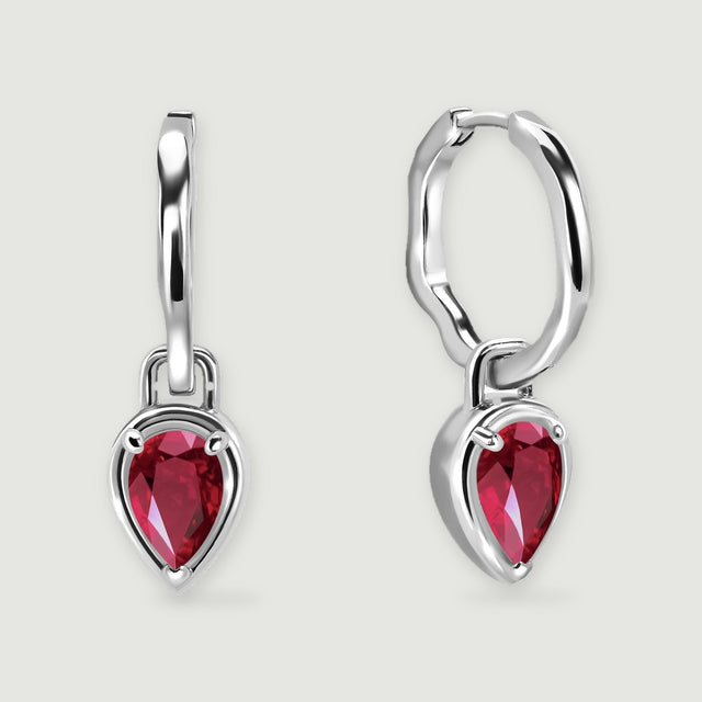 Two white rhodium plated hoop earrings display red pear-shaped stones above soft shadows.
