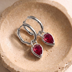 White rhodium plated ruby earrings lie side by side on a softly lit stone surface.