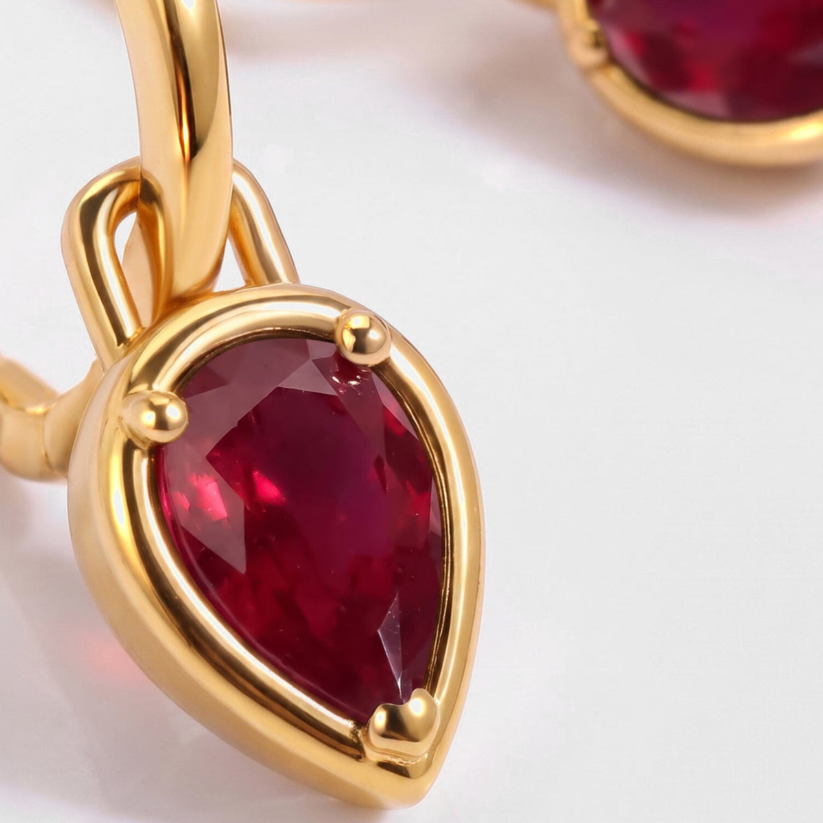 A close view shows the red ruby facets, three rounded prongs, and yellow gold plated setting.