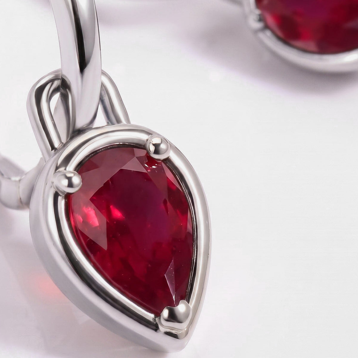 The pear-shaped red stone and polished white rhodium plated hoop fill this close view.
