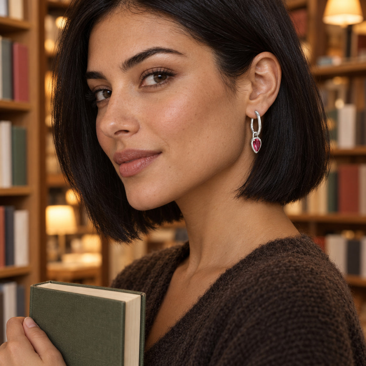 A woman with a black bob wears a white rhodium plated ruby hoop while holding a book in a bookshop.