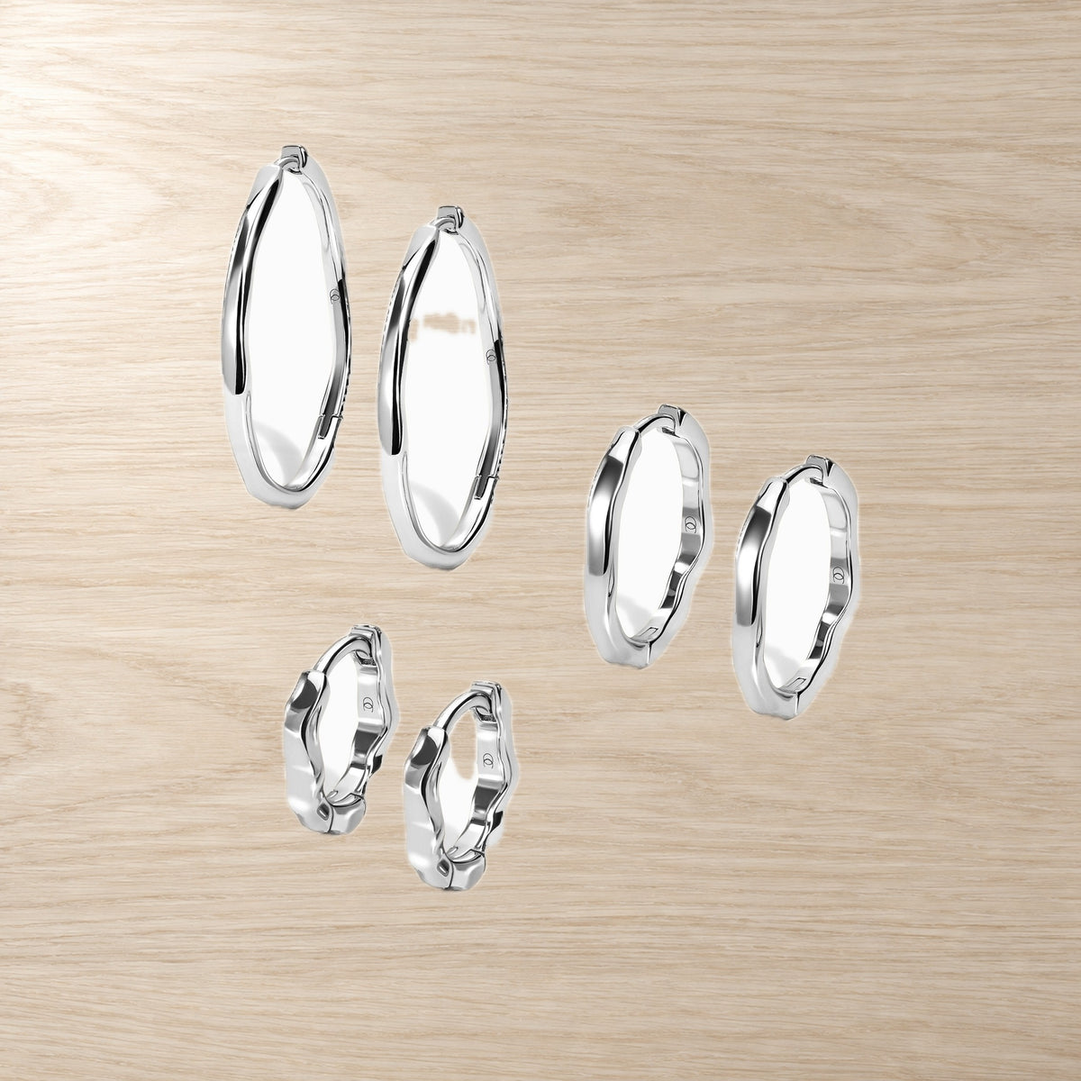 Set of three pairs of smooth, wavy hoop earrings in graduated sizes on a wood surface.