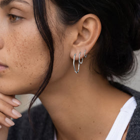 Close-up of a freckled person wearing three graduated wavy hoops on one ear.