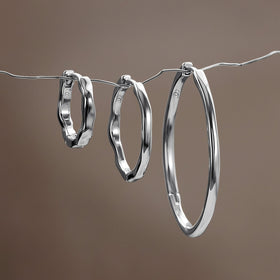 Three graduated wavy hoop earrings hang from a thin wire against a softly blurred brown background.
