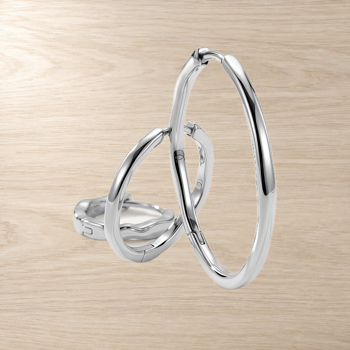 Three graduated wavy hoop earrings overlap in a layered arrangement on a light wood surface.