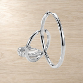 Three graduated wavy hoop earrings overlap in a layered arrangement on a light wood surface.
