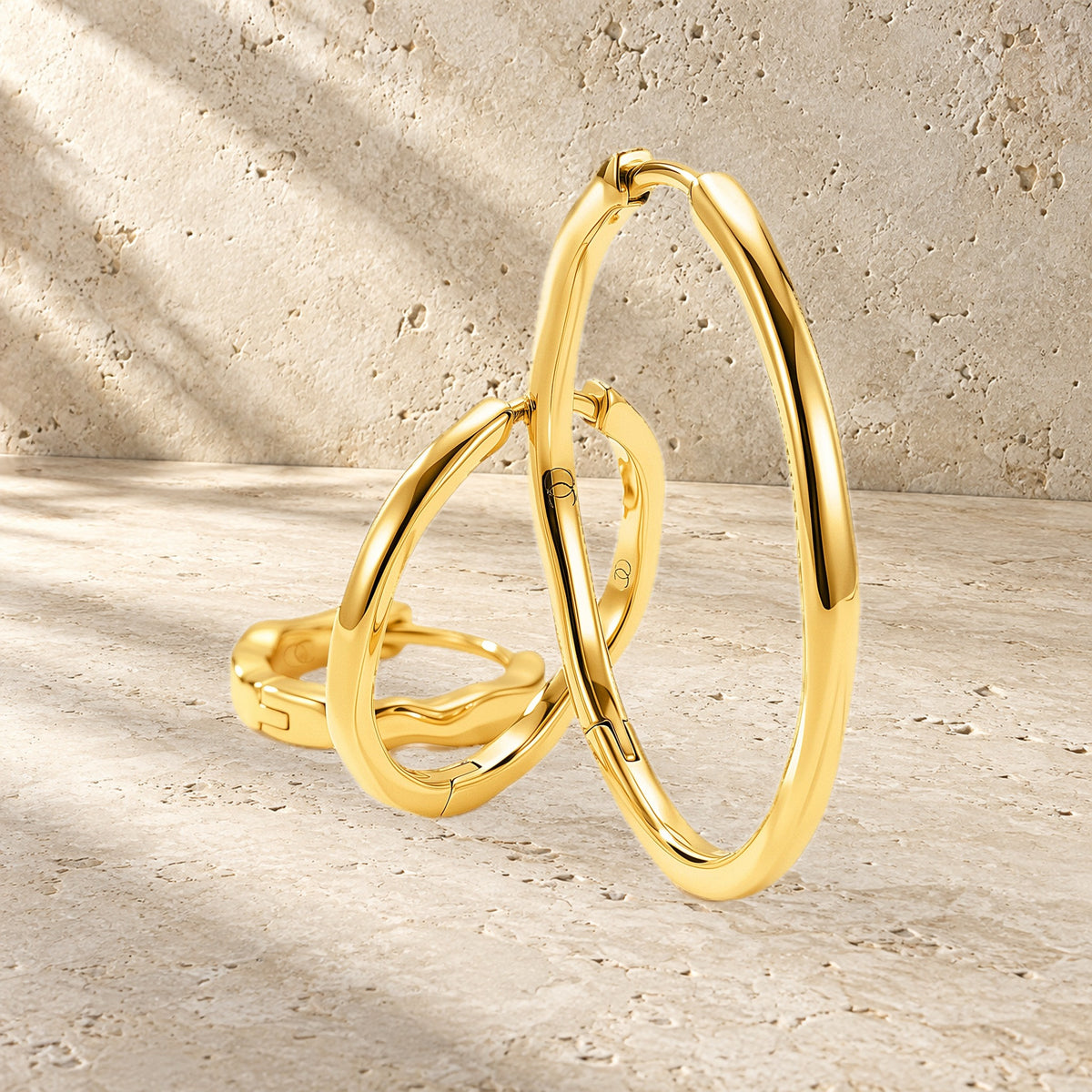 Three graduated wavy hoop earrings are arranged on a textured stone surface in warm light.