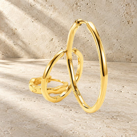Three graduated wavy hoop earrings are arranged on a textured stone surface in warm light.