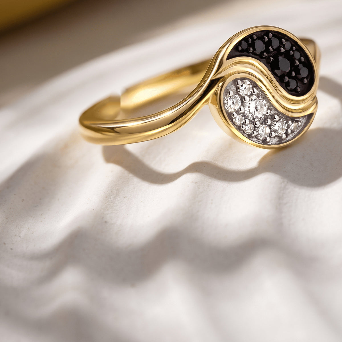A yellow gold plated ring rests at an angle on a pale stone surface with a sunlit shadow.