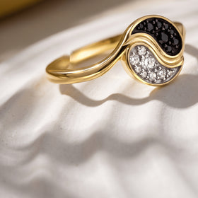 A yellow gold plated ring rests at an angle on a pale stone surface with a sunlit shadow.