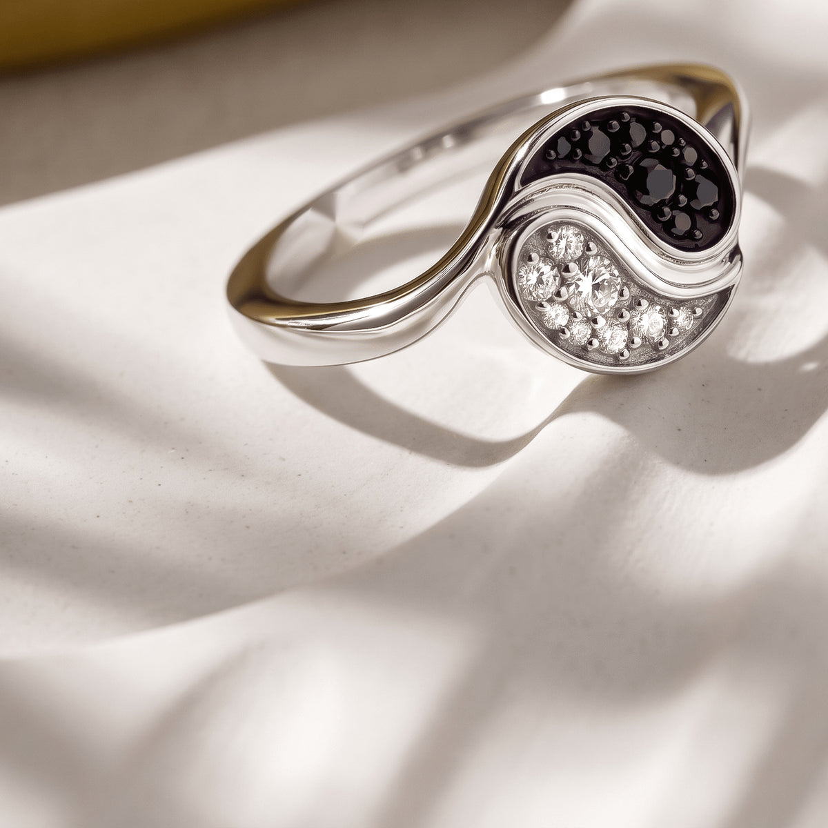 A rhodium plated ring rests on a clean pale surface with its curved band and stone face visible.