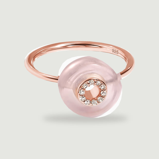 A rose gold vermeil ring displays a translucent pink disc and a sparkling circular center on a light gray surface.