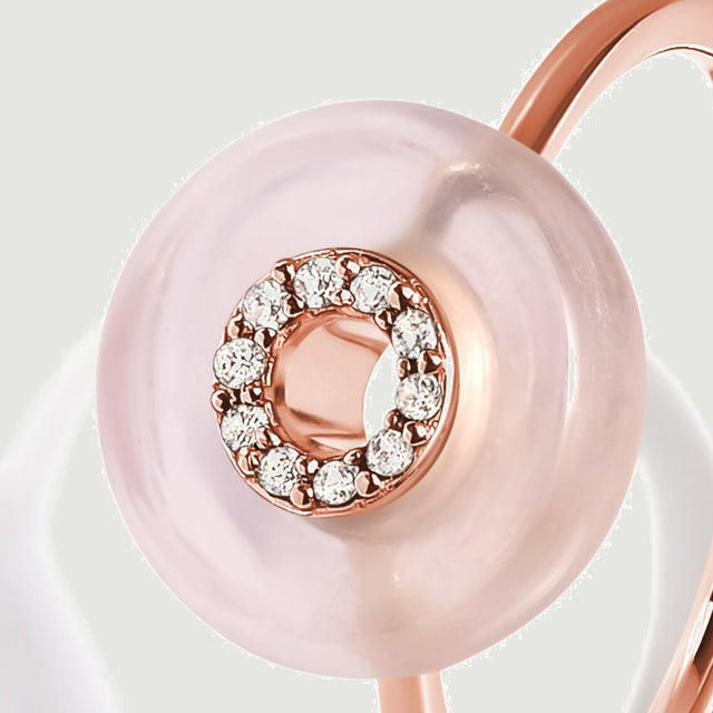 A pale pink stone surrounds a rose gold circular center set with clear stones in this angled close view.