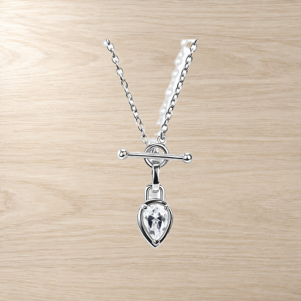 Close-up of a chain necklace with a pear-shaped clear gemstone and horizontal T-bar pendant on wood.