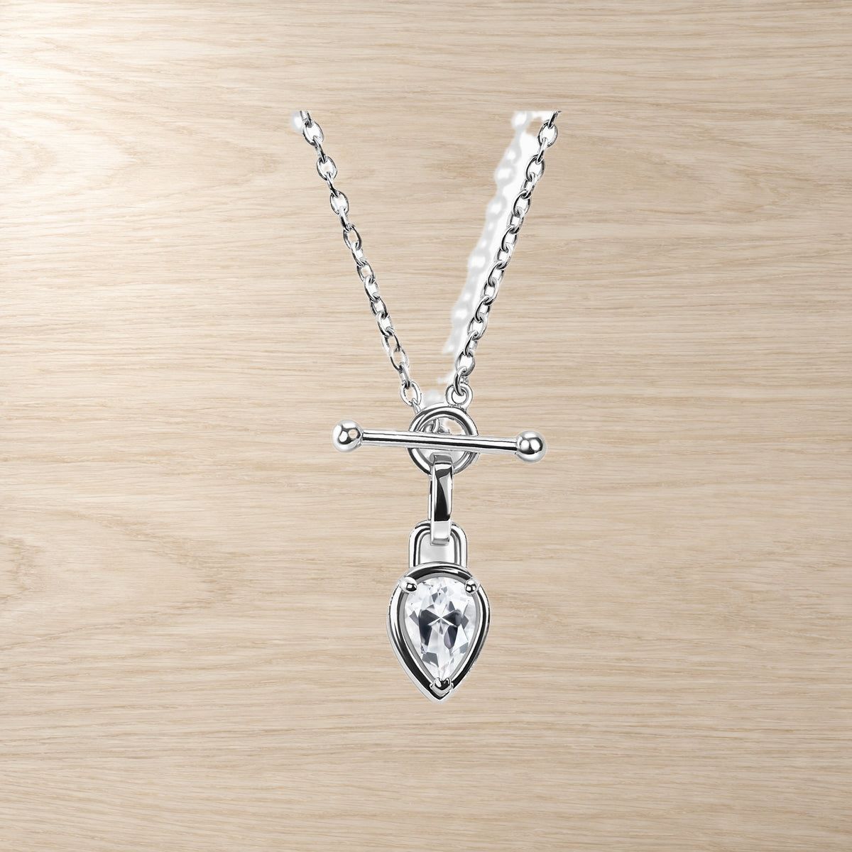 Close-up of a chain necklace with a pear-shaped clear gemstone and horizontal T-bar pendant on wood.